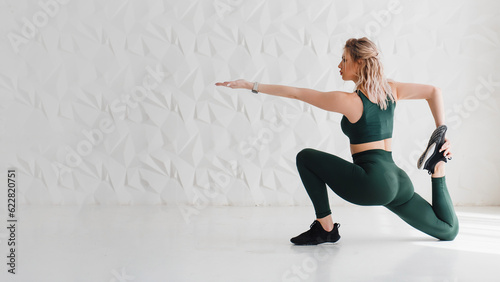 Beautiful sporty woman in crop top and green leggings doing stretching for legs