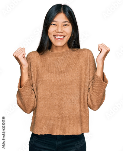 Beautiful young asian woman wearing casual winter sweater celebrating surprised and amazed for success with arms raised and open eyes. winner concept.
