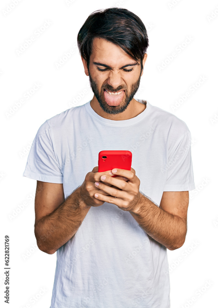 Hispanic man with blue eyes using smartphone typing message sticking tongue out happy with funny expression. Hispanic man with blue eyes using smartphone typing message sticking tongue out happy with funny expression.
