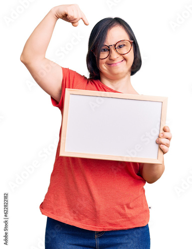 Brunette woman with down syndrome holding empty white chalkboard pointing finger to one self smiling happy and proud