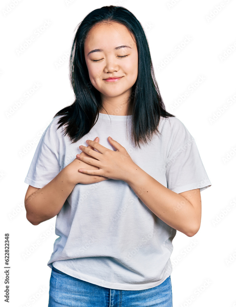 Young chinese woman wearing casual white t shirt smiling with hands on chest with closed eyes and grateful gesture on face. health concept. Young chinese woman wearing casual white t shirt smiling with hands on chest with closed eyes and grateful gesture on face. health concept.