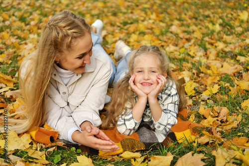 The family has fun in the park. Girl and mother lie on a blanket, the girl looks at the camera and smiles