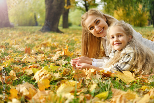 The family spends time together in the park. Girl and mother lie on a blanket, smile and look at the camera