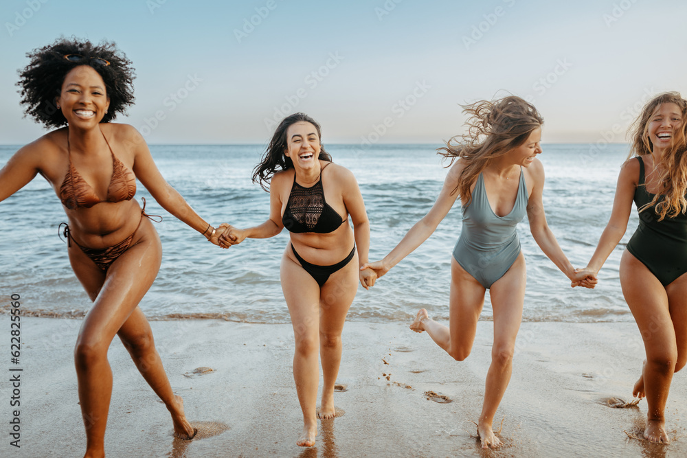 Overjoyed female friends in swimwear having fun and running on the beach, laughing and enjoying their summer vacation Overjoyed female friends in swimwear having fun and running on the beach, laughing and enjoying their summer vacation