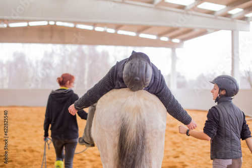 Hippotherapy assistance therapist with medical disability patient on equestrian riding hall.