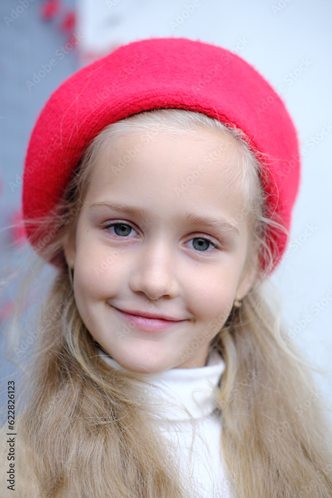 Portrait of a beautiful little girl in a trench coat and a red beret. A girl poses while sitting at a table in a street cafe. Portrait of a beautiful little girl in a trench coat and a red beret. A girl poses while sitting at a table in a street cafe.