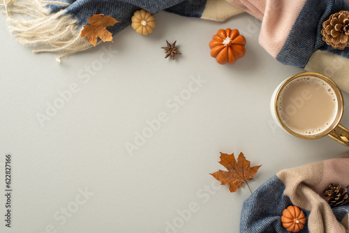 Cozy fall vibes at home: High angle view of a warm patchy blanket, maple leaves, pumpkin candles and aromatic spices with ample space for text or advertising on a light grey isolated background