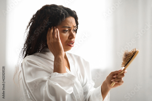 Shocked Black Woman Looking At Brush Full Of Fallen Hair At Home