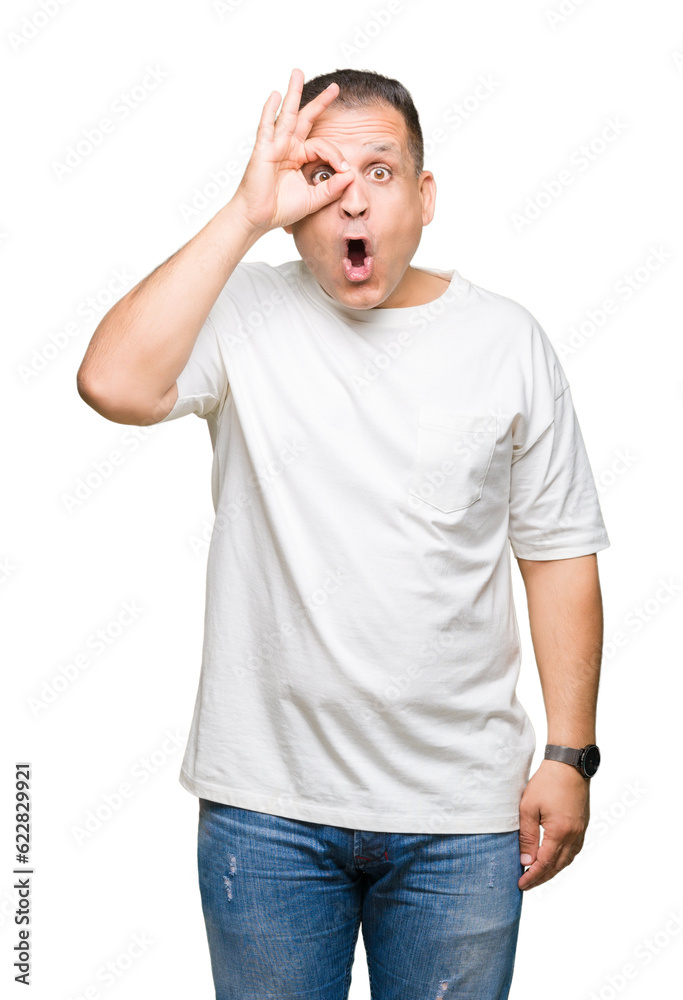 Middle age arab man wearig white t-shirt over isolated background doing ok gesture shocked with surprised face, eye looking through fingers. Unbelieving expression. Middle age arab man wearig white t-shirt over isolated background doing ok gesture shocked with surprised face, eye looking through fingers. Unbelieving expression.