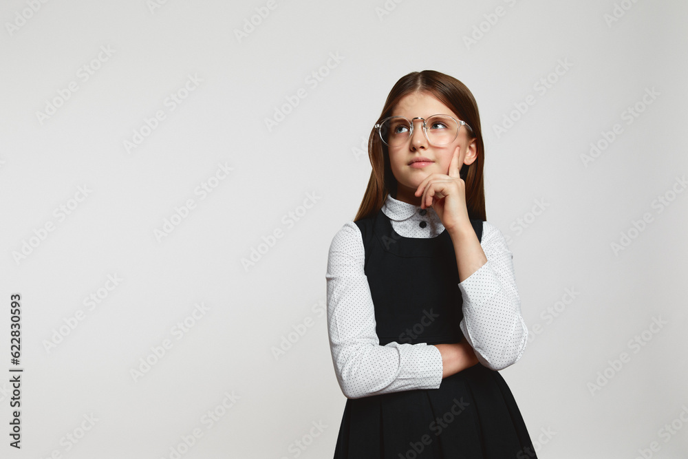 Schoolgirl standing with thoughtful serious smart expression, pondering answer, having doubts and suspicion, wearing school uniform against white Schoolgirl standing with thoughtful serious smart expression, pondering answer, having doubts and suspicion, wearing school uniform against white