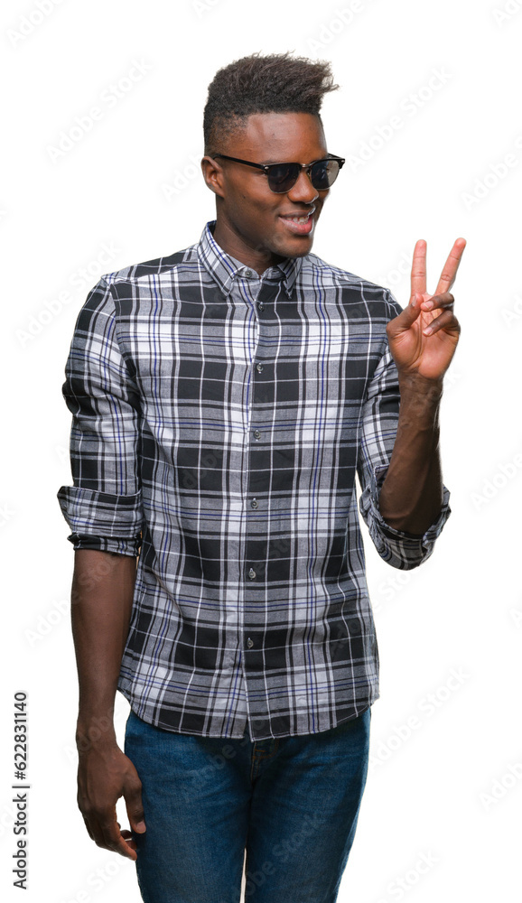 Young african american man wearing sunglasses over isolated background smiling with happy face winking at the camera doing victory sign. Number two. Young african american man wearing sunglasses over isolated background smiling with happy face winking at the camera doing victory sign. Number two.