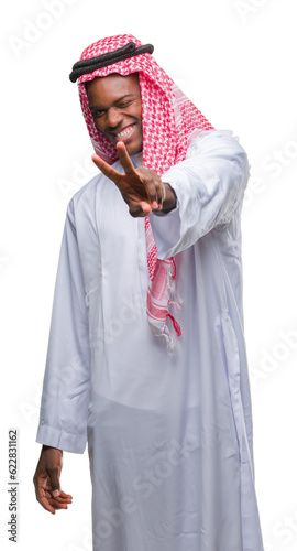 Young arabic african man wearing traditional keffiyeh over isolated background smiling looking to the camera showing fingers doing victory sign. Number two.