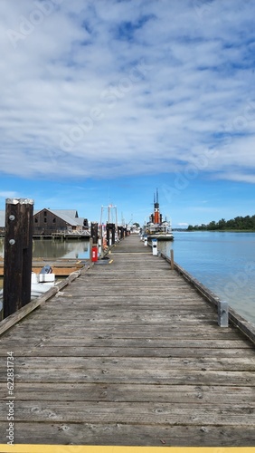 Wooden dock towards barn house and ship with blue sky and white clouds. 