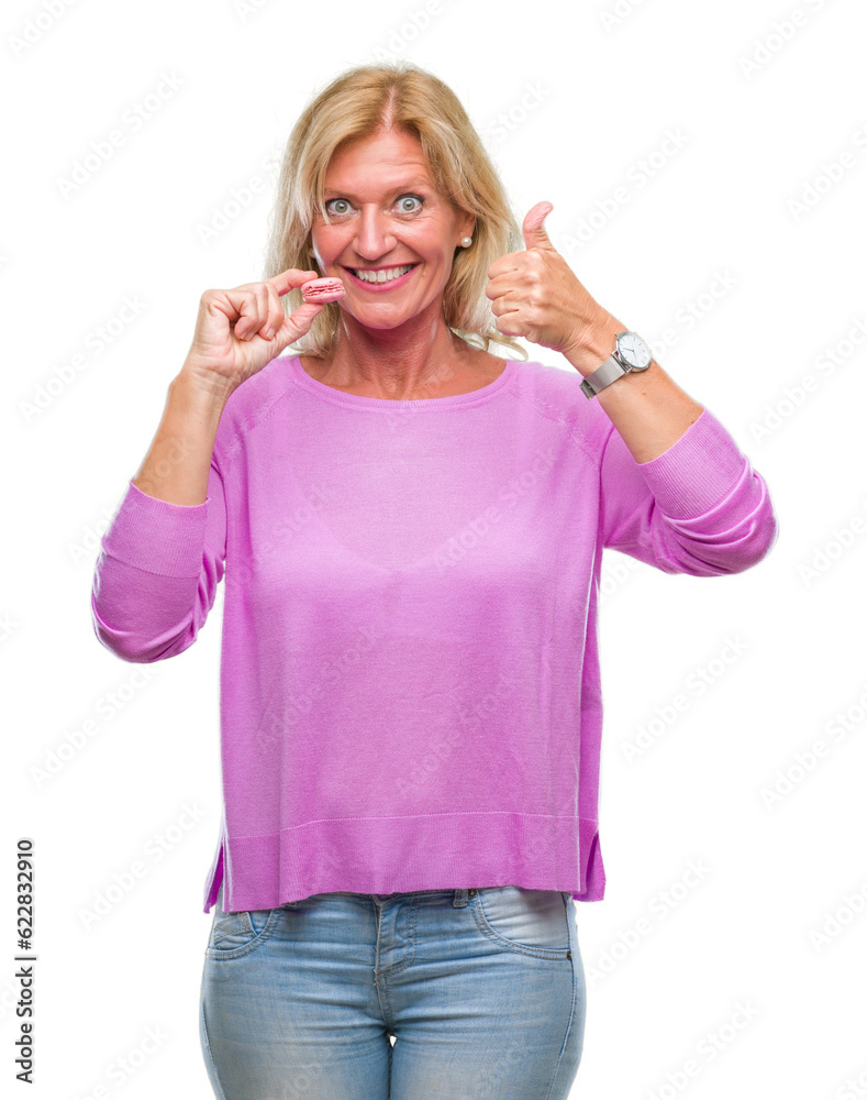 Middle age blonde woman eatin pink macaron biscuit over isolated background happy with big smile doing ok sign, thumb up with fingers, excellent sign Middle age blonde woman eatin pink macaron biscuit over isolated background happy with big smile doing ok sign, thumb up with fingers, excellent sign