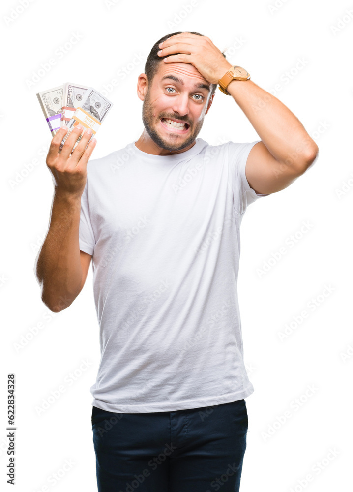 Young handsome man holding stack of dollars over isolated background stressed with hand on head, shocked with shame and surprise face, angry and frustrated. Fear and upset for mistake. Young handsome man holding stack of dollars over isolated background stressed with hand on head, shocked with shame and surprise face, angry and frustrated. Fear and upset for mistake.