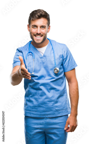 Young handsome doctor surgeon man over isolated background smiling friendly offering handshake as greeting and welcoming. Successful business. © Krakenimages.com