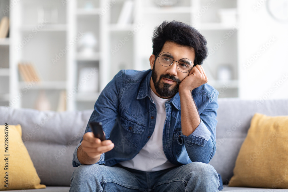 Fototapeta premium Portrait Of Bored Young Eastern Man Watching TV At Home