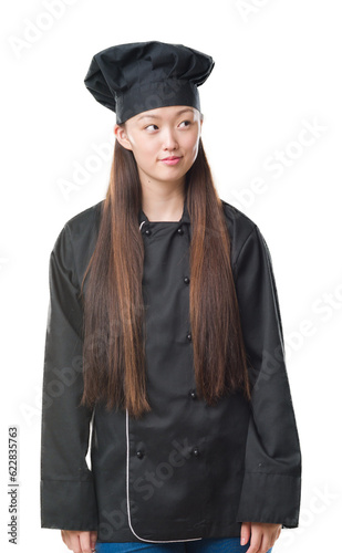Young Chinese woman over isolated background wearing chef uniform smiling looking side and staring away thinking.