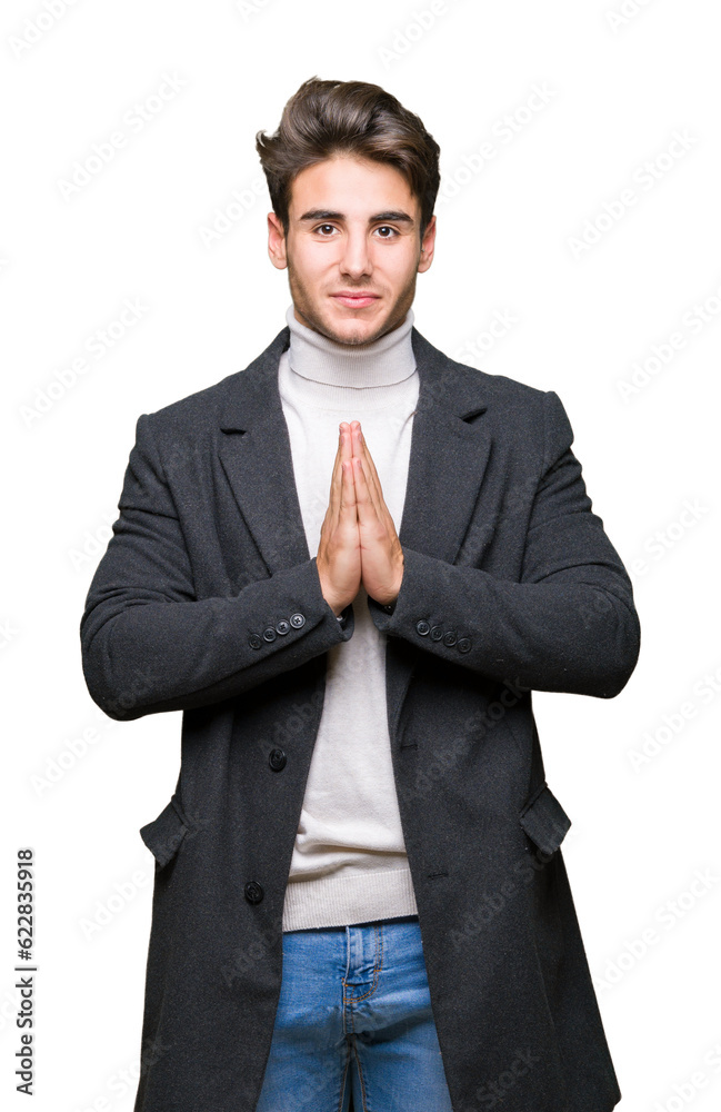 Young elegant man wearing winter coat over isolated background praying with hands together asking for forgiveness smiling confident.