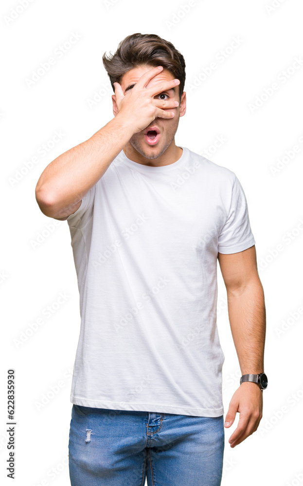 Young handsome man wearing white t-shirt over isolated background peeking in shock covering face and eyes with hand, looking through fingers with embarrassed expression. Young handsome man wearing white t-shirt over isolated background peeking in shock covering face and eyes with hand, looking through fingers with embarrassed expression.