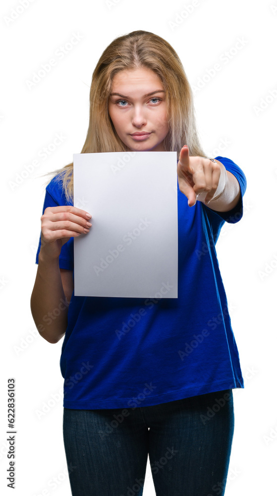 Young caucasian woman holding blank paper sheet over isolated background pointing with finger to the camera and to you, hand sign, positive and confident gesture from the front Young caucasian woman holding blank paper sheet over isolated background pointing with finger to the camera and to you, hand sign, positive and confident gesture from the front