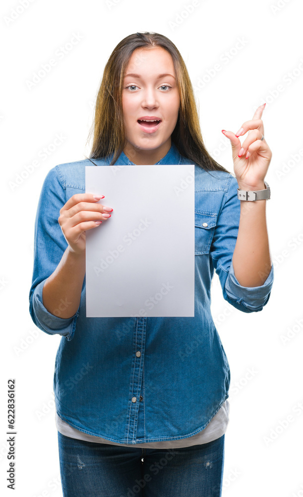 Young caucasian woman holding blank paper sheet over isolated background surprised with an idea or question pointing finger with happy face, number one Young caucasian woman holding blank paper sheet over isolated background surprised with an idea or question pointing finger with happy face, number one