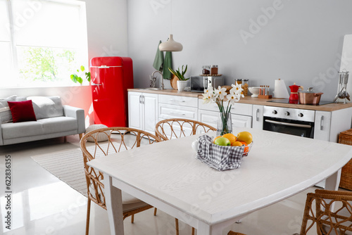 Basket with fruits and narcissus flowers on table in light kitchen