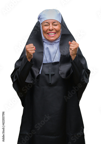 Middle age senior christian catholic nun woman over isolated background excited for success with arms raised celebrating victory smiling. Winner concept.