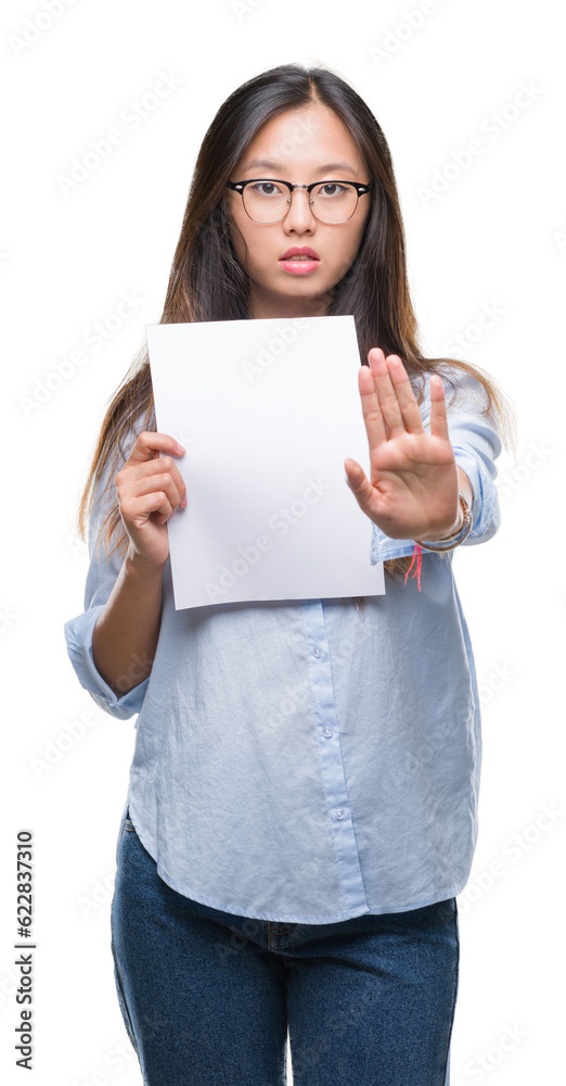 Young asian woman holding blank paper over isolated background with open hand doing stop sign with serious and confident expression, defense gesture Young asian woman holding blank paper over isolated background with open hand doing stop sign with serious and confident expression, defense gesture
