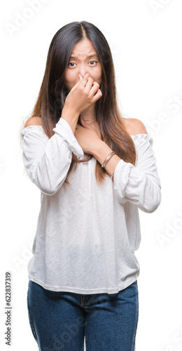 Young asian woman over isolated background smelling something stinky and disgusting, intolerable smell, holding breath with fingers on nose. Bad smells concept. photo