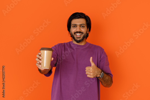 Positive happy young eastern guy showing takaway coffee photo