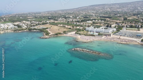 Corallia Beach on the island of Cyprus, located in the town of Peja near Paphos. A bird's-eye view captures the stunning, pristine blue waters of the Mediterranean Sea. 