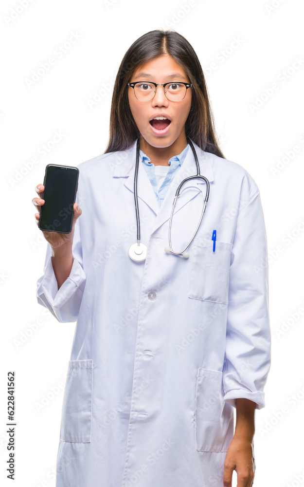 Young asian doctor woman holding smartphone over isolated background scared in shock with a surprise face, afraid and excited with fear expression Young asian doctor woman holding smartphone over isolated background scared in shock with a surprise face, afraid and excited with fear expression
