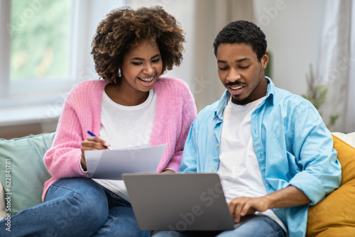 Happy young black couple filling papers and using laptop