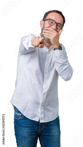 Handsome middle age elegant senior business man wearing glasses over isolated background Laughing of you, pointing to the camera with finger hand over mouth, shame expression