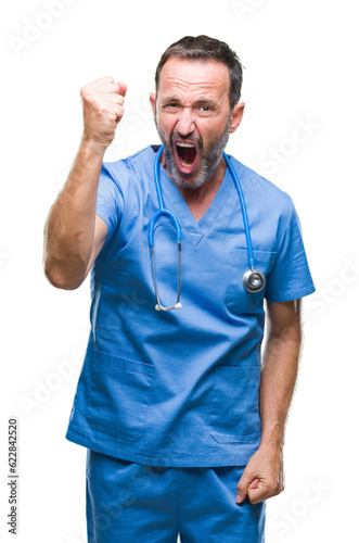 Middle age hoary senior doctor man wearing medical uniform over isolated background angry and mad raising fist frustrated and furious while shouting with anger. Rage and aggressive concept. © Krakenimages.com