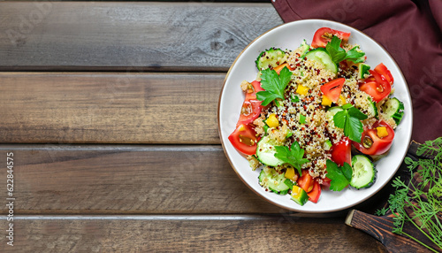 Fresh healthy salad with quinoa, colorful tomatoes, sweet pepper, cucumber and parsley on wooden background top view. Food and health. Superfood meal. Space for text.