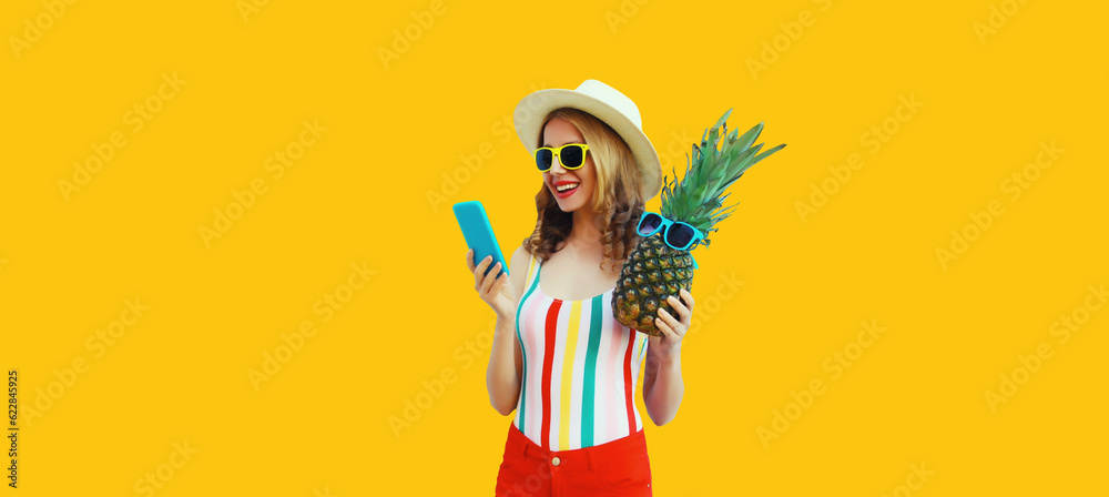 Summer portrait of stylish happy young woman with smartphone and fresh pineapple wearing straw hat, sunglasses on yellow background Summer portrait of stylish happy young woman with smartphone and fresh pineapple wearing straw hat, sunglasses on yellow background