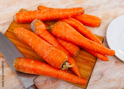 Bunch of fresh orange carrots on wooden cutting board. Preparing food.