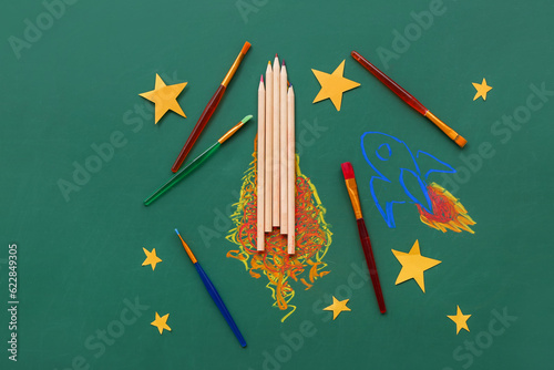 Creative composition with drawn rockets, stars and different stationery on green chalkboard