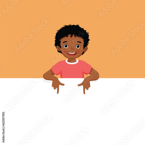 Little African boy standing behind blank board pointing to empty banner with finger