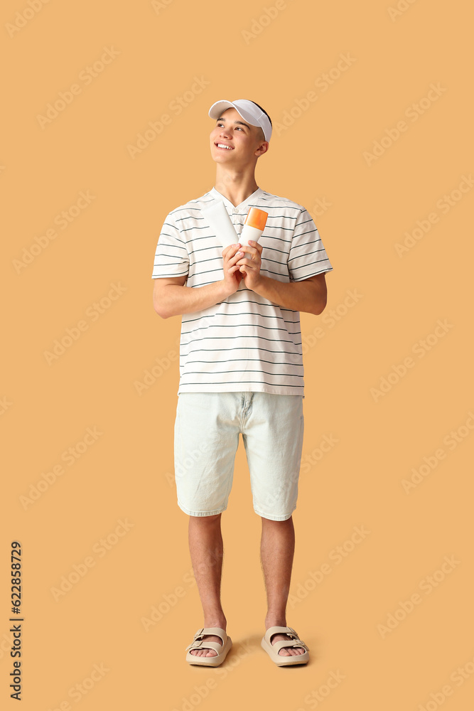 Happy young man with bottles of sunscreen cream on orange background