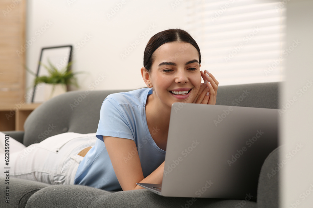 Naklejka premium Happy woman working with laptop on sofa at home