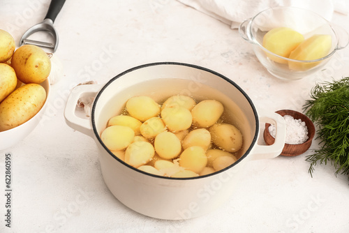 Pot with raw potatoes on light background