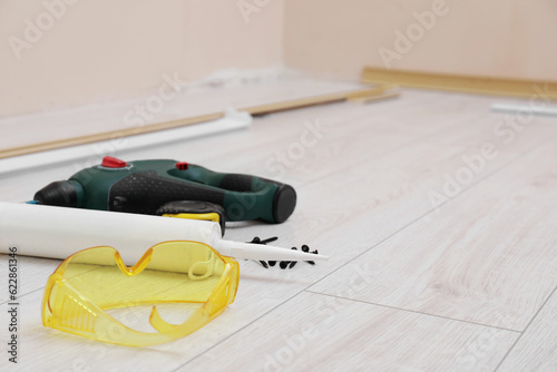 Plinths, caulking gun, screwdriver, protective glasses and screws on laminated floor in room