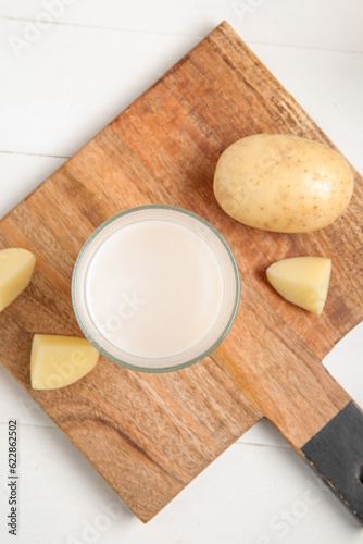 Glass of tasty potato milk on white wooden background