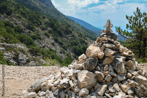 Stack pyramide of stones on top of mountain on background of mountains covered with forests. Croatia, Bol island. Concept of balance and harmony. Stack of zen stones. Teamwork balance concept © Lyudmila