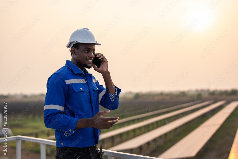 Obraz premium African young engineer talking on phone while work at solar cell field.