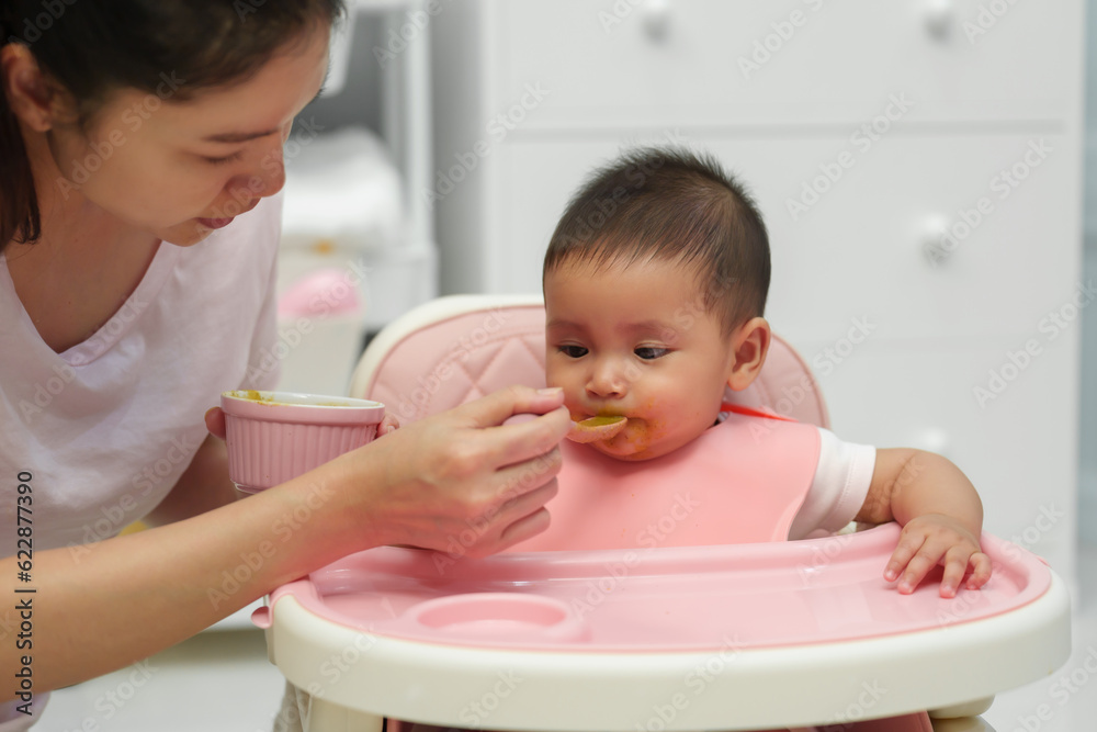 mother feeding food to her infant baby eating with spoon at home mother feeding food to her infant baby eating with spoon at home