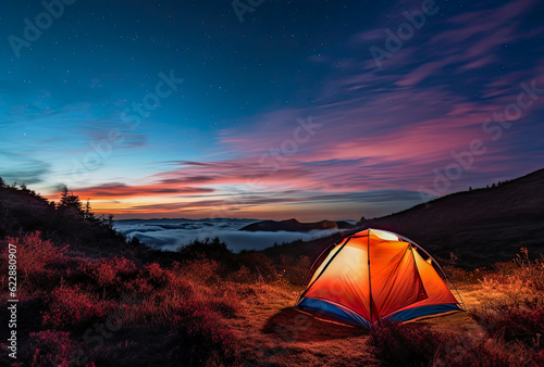 An illuminated tent in the mountains with great views of a lake. Camping is a great way to get closer to nature and enjoy a summer vacation.
